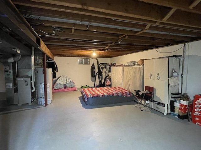 unfinished basement featuring visible vents, heating unit, and water heater