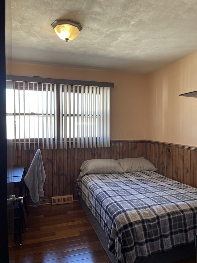 bedroom featuring visible vents, hardwood / wood-style flooring, a textured ceiling, wooden walls, and wainscoting