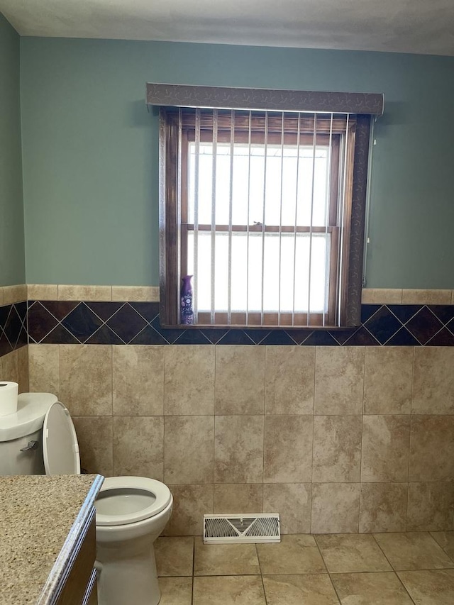 half bathroom featuring tile patterned flooring, tile walls, toilet, and visible vents