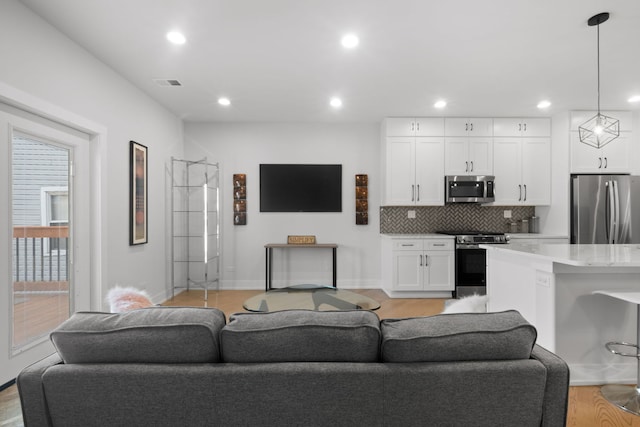 living room with recessed lighting, visible vents, light wood finished floors, and baseboards