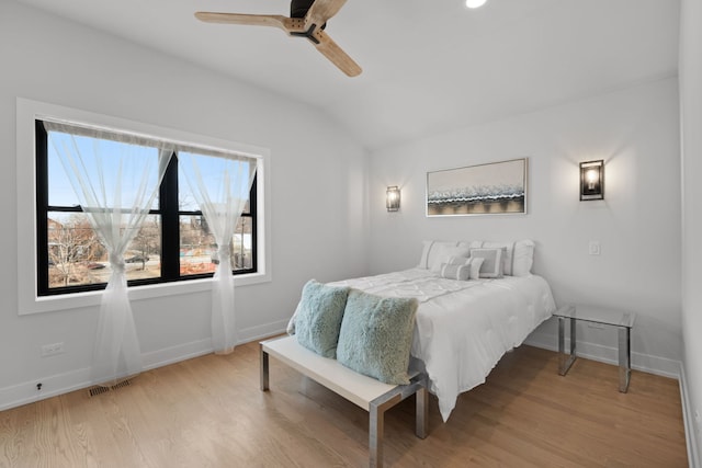 bedroom with a ceiling fan, visible vents, baseboards, light wood finished floors, and vaulted ceiling