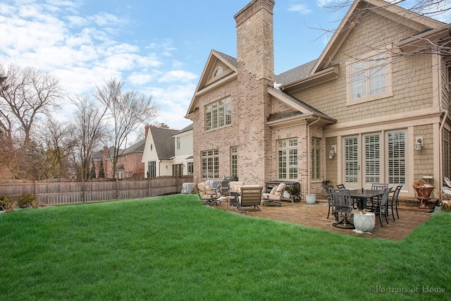 rear view of property featuring a patio area, a lawn, fence, and a chimney