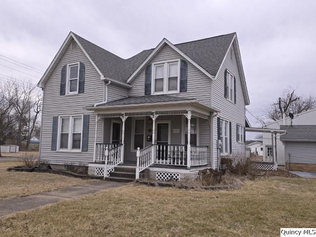 view of front facade with covered porch, a shingled roof, and a front lawn