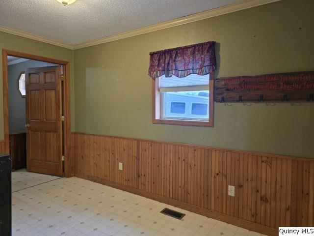 unfurnished room featuring visible vents, wainscoting, wood walls, a textured ceiling, and tile patterned floors