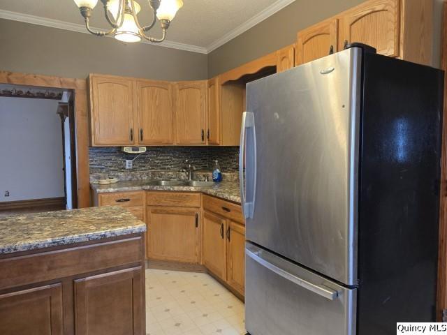 kitchen with a notable chandelier, crown molding, freestanding refrigerator, and a sink