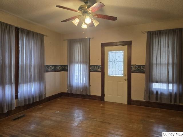 foyer entrance featuring wainscoting, wood finished floors, visible vents, and ceiling fan