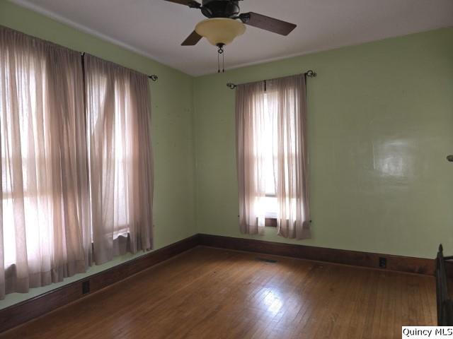 spare room featuring baseboards, wood finished floors, and a ceiling fan