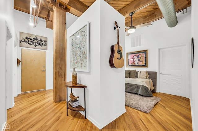 corridor with light wood finished floors, visible vents, beamed ceiling, and baseboards