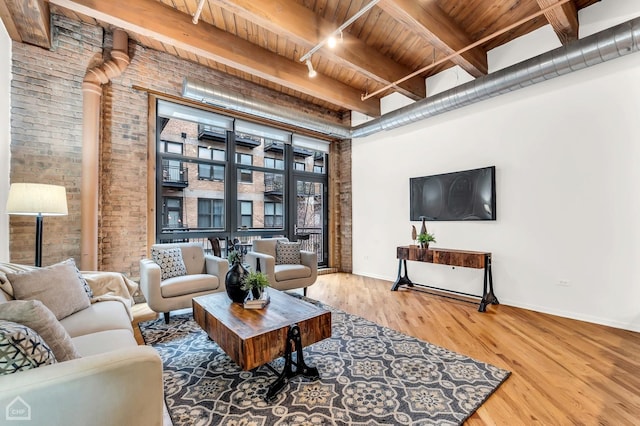 living room featuring beam ceiling, wood finished floors, wooden ceiling, brick wall, and rail lighting