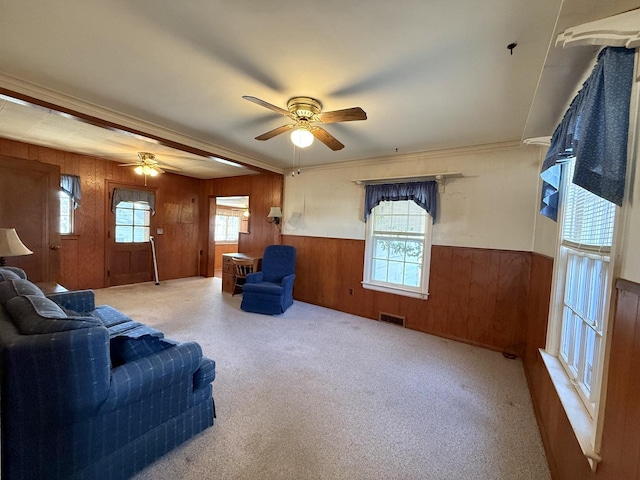 carpeted living area with ceiling fan, visible vents, plenty of natural light, and a wainscoted wall