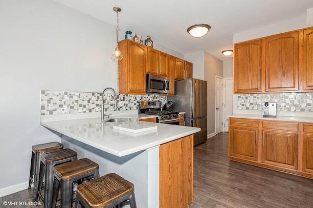 kitchen featuring a peninsula, a sink, stainless steel appliances, light countertops, and a kitchen bar