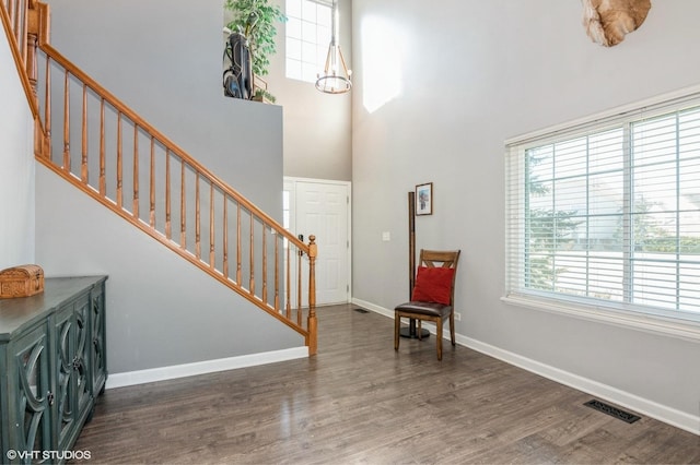 foyer entrance featuring visible vents, baseboards, stairs, a towering ceiling, and wood finished floors