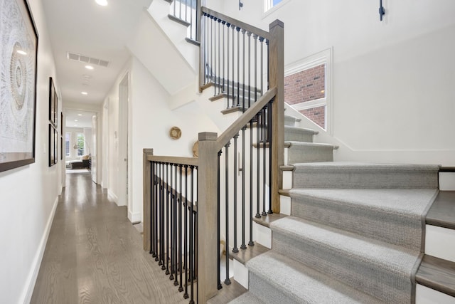 stairway featuring visible vents, wood finished floors, recessed lighting, a high ceiling, and baseboards