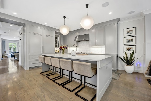 kitchen featuring gray cabinetry, wall chimney range hood, tasteful backsplash, wood finished floors, and light countertops