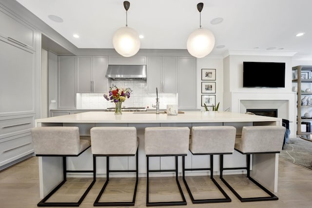 kitchen with a sink, decorative backsplash, a kitchen bar, wall chimney range hood, and open floor plan