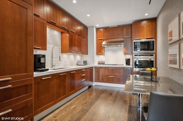 kitchen featuring ventilation hood, built in microwave, dark wood finished floors, stainless steel oven, and a sink