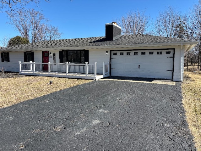 ranch-style house featuring a shingled roof, covered porch, a chimney, a garage, and driveway