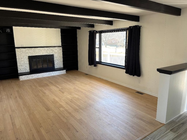 unfurnished living room with visible vents, beamed ceiling, a fireplace, light wood finished floors, and baseboards