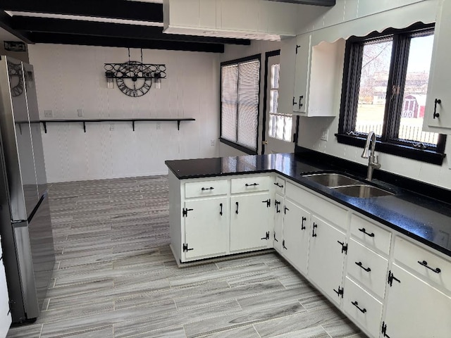 kitchen featuring dark countertops, a peninsula, freestanding refrigerator, white cabinetry, and a sink