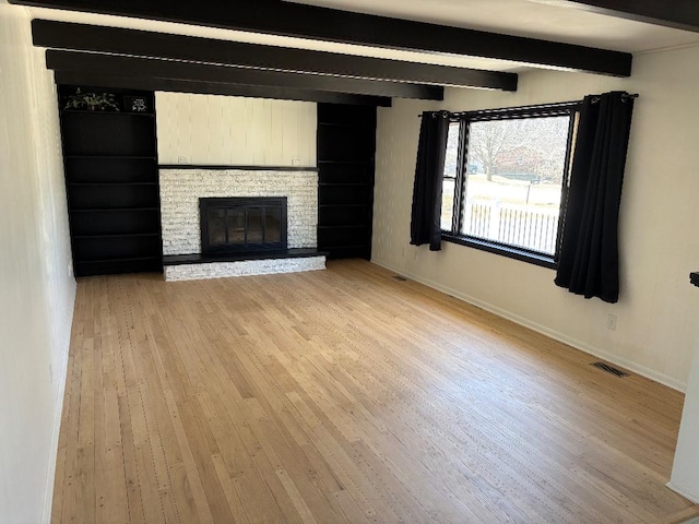 unfurnished living room featuring visible vents, a brick fireplace, baseboards, beamed ceiling, and light wood-style flooring