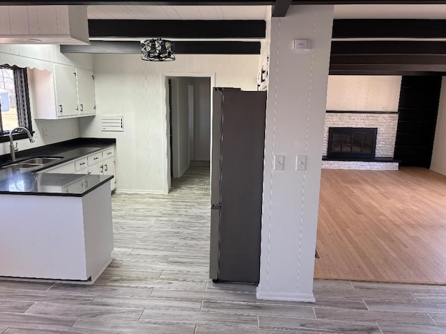 kitchen with beam ceiling, a sink, dark countertops, freestanding refrigerator, and white cabinets