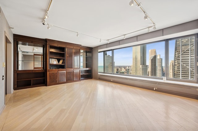 unfurnished living room featuring a city view, track lighting, and light wood-type flooring