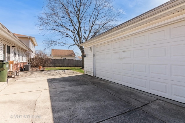 garage featuring concrete driveway, central air condition unit, and fence