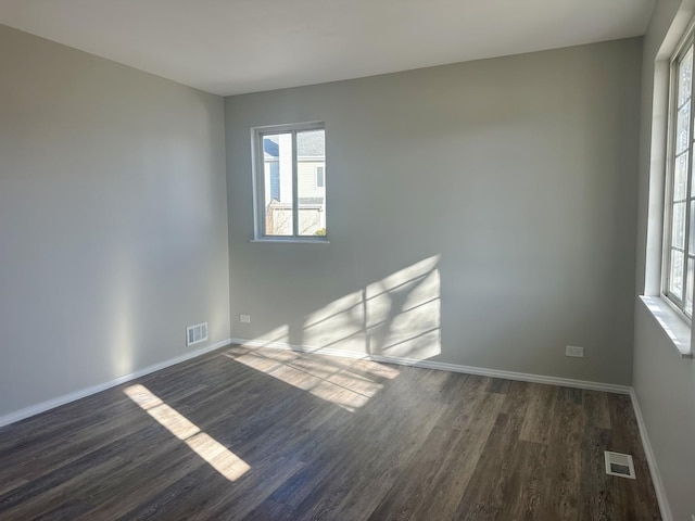 spare room with dark wood finished floors, visible vents, and plenty of natural light