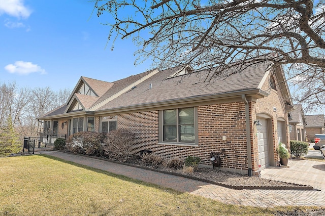 view of side of home with a yard, roof with shingles, concrete driveway, an attached garage, and brick siding