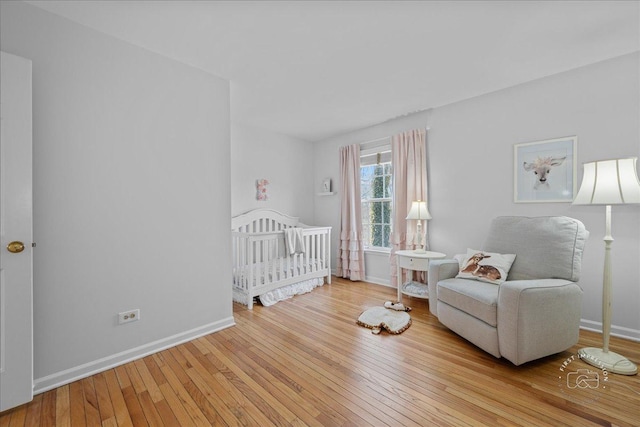 bedroom with a crib, baseboards, and hardwood / wood-style flooring