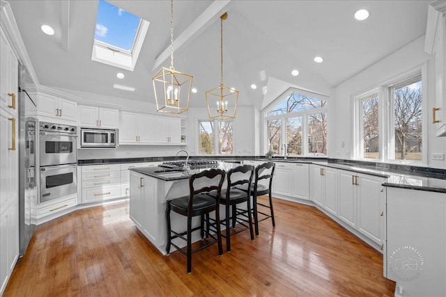 kitchen with vaulted ceiling with skylight, an island with sink, white cabinets, and appliances with stainless steel finishes