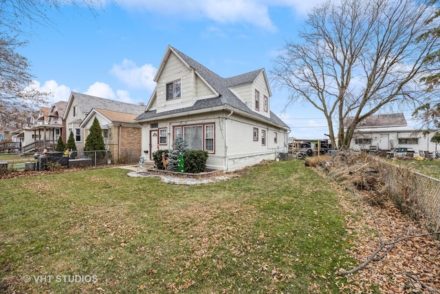 view of front facade featuring a front yard, a fenced backyard, and a shingled roof