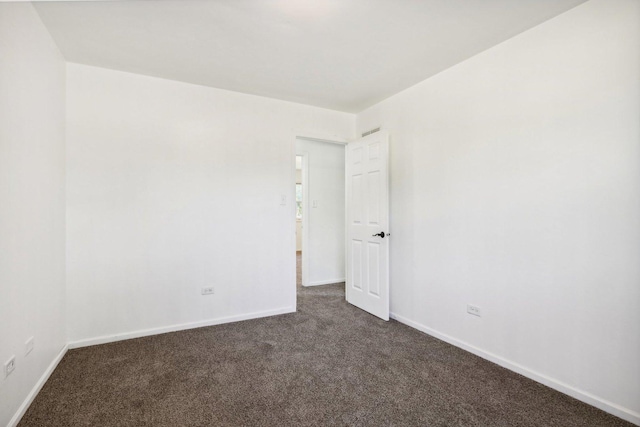 spare room featuring baseboards and dark colored carpet