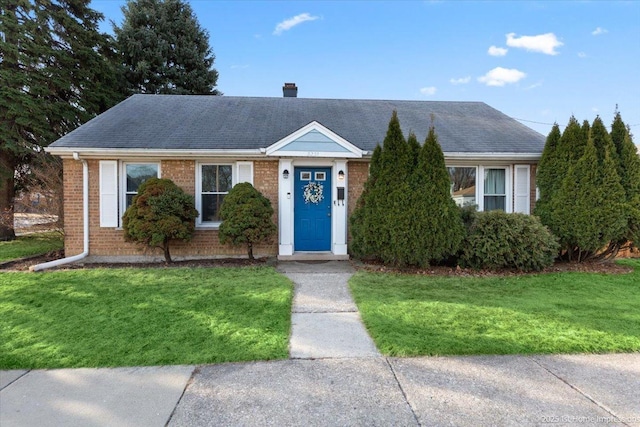 ranch-style home with a front yard, brick siding, roof with shingles, and a chimney