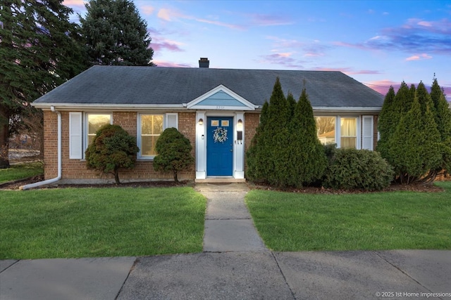 single story home with brick siding, a chimney, a front yard, and roof with shingles