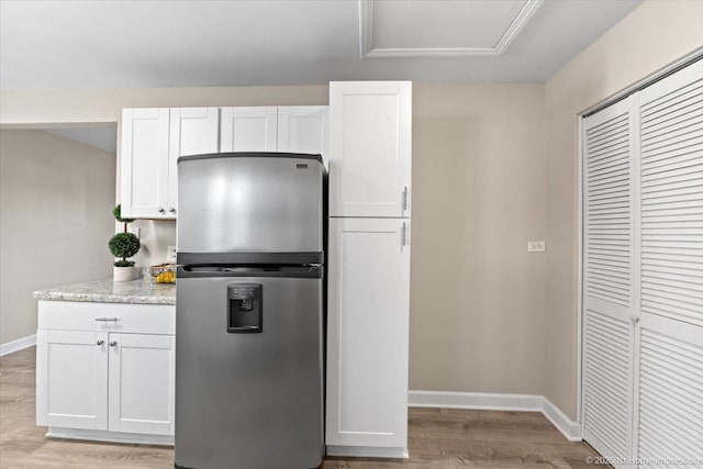 kitchen featuring light stone countertops, baseboards, light wood-style flooring, stainless steel fridge with ice dispenser, and white cabinetry