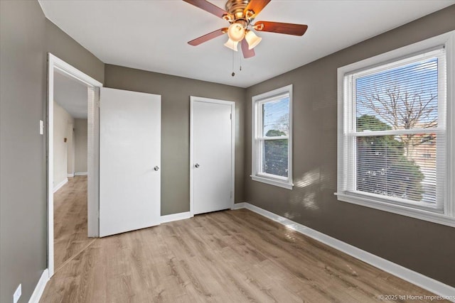 unfurnished bedroom with ceiling fan, light wood-type flooring, and baseboards