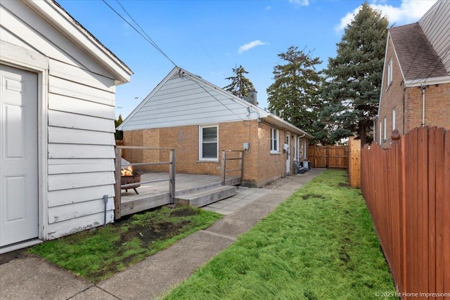 exterior space with brick siding, a deck, a yard, and fence