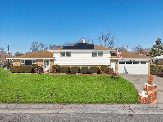 tri-level home featuring concrete driveway, a garage, a front lawn, and roof mounted solar panels