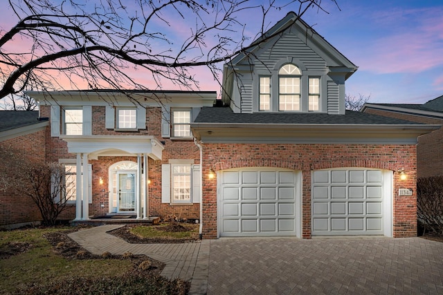 traditional home with decorative driveway, brick siding, and a shingled roof