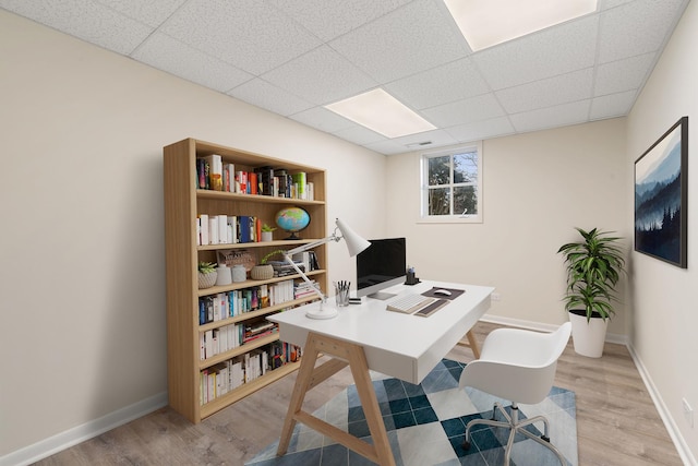 office area featuring light wood-style flooring, a paneled ceiling, and baseboards