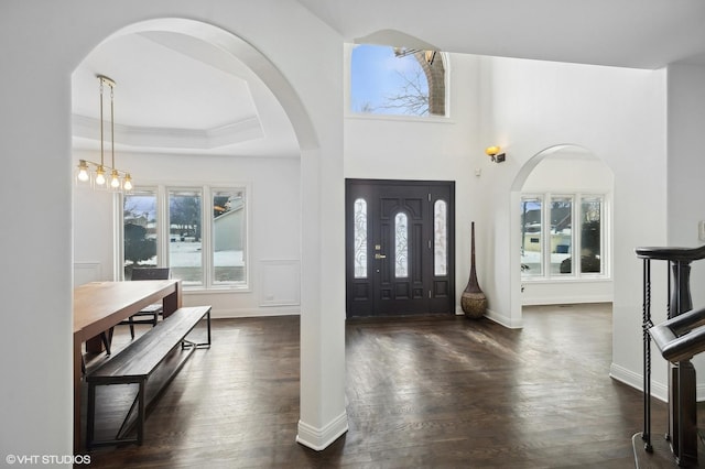 entrance foyer featuring crown molding, a raised ceiling, baseboards, and dark wood-style flooring