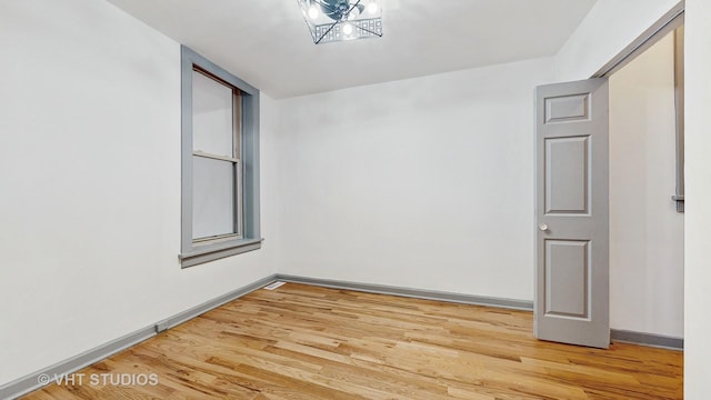 empty room featuring baseboards, a notable chandelier, and light wood finished floors