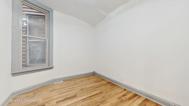 unfurnished room with visible vents, baseboards, wood finished floors, and vaulted ceiling