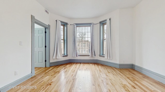 spare room with wood finished floors, visible vents, and baseboards