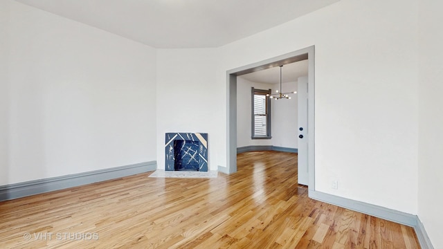 unfurnished living room featuring light wood-type flooring, baseboards, and an inviting chandelier