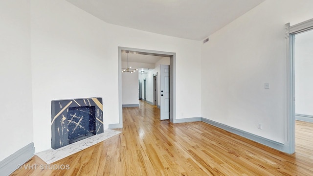 unfurnished living room featuring an inviting chandelier, wood finished floors, and baseboards