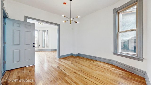 interior space with light wood finished floors, a notable chandelier, and baseboards