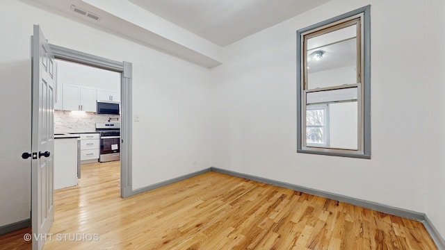 unfurnished room featuring light wood-type flooring, visible vents, and baseboards