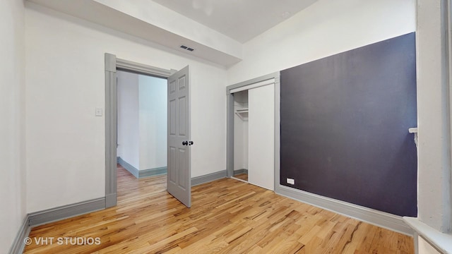 unfurnished bedroom with a closet, visible vents, light wood-type flooring, and baseboards